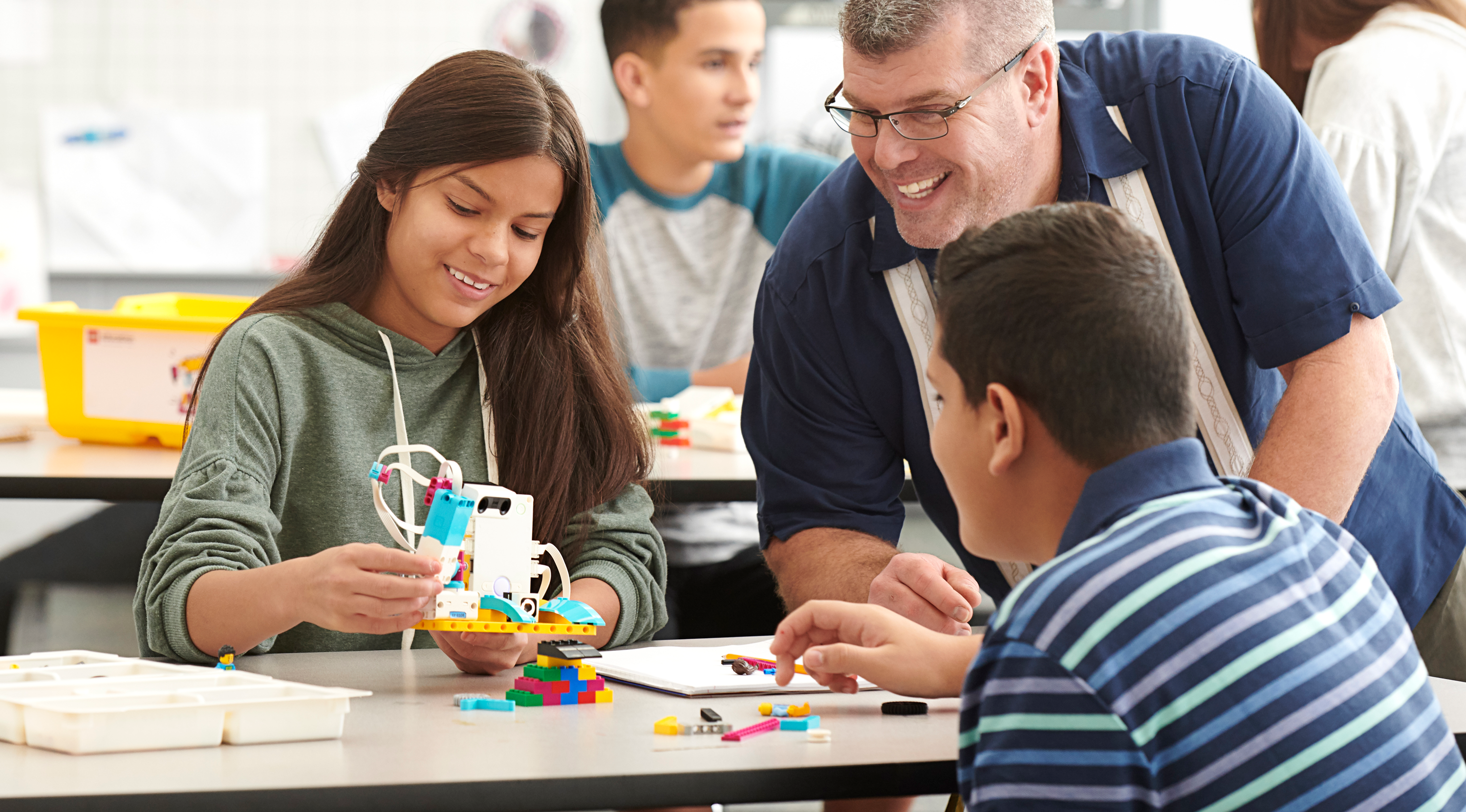 Male teacher showing a teen girl and boy how their LEGO EDUCATION SPIKE Prime set to build robotics.